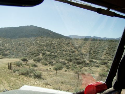 1967 Ford Bronco - View from inside a vehicle traveling through a desolate, hilly terrain with sparse vegetation and a distant mountain range.
