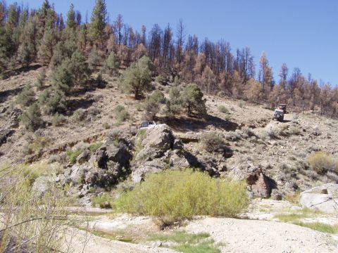 1967 Ford Bronco - Two off-road vehicles traverse a challenging, arid landscape with sparse vegetation and evidence of a past wildfire.