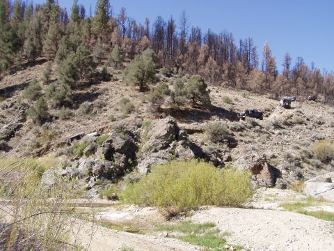 1967 Ford Bronco - Multiple off-road vehicles ascend a challenging, dry, rocky slope with burnt trees in the background.