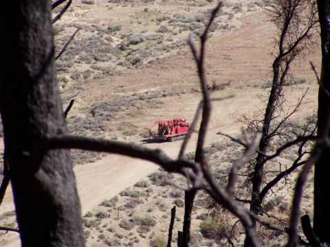 1967 Ford Bronco - A large red industrial vehicle with tracks moves along a dirt road through a dry, arid landscape.