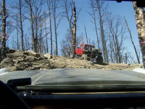 1967 Ford Bronco - Off-road pickup truck navigating a rocky trail through a forest with burnt trees.