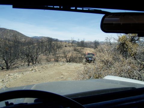 1967 Ford Bronco - Multiple off-road vehicles navigate a dusty trail in a post-fire landscape.