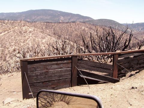 1967 Ford Bronco - Post-fire landscape shows a damaged wooden fence and barren hills under a clear sky.