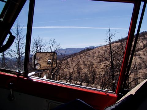 1967 Ford Bronco - View from inside a red vehicle shows a side mirror reflecting another vehicle against a backdrop of a burnt landscape.