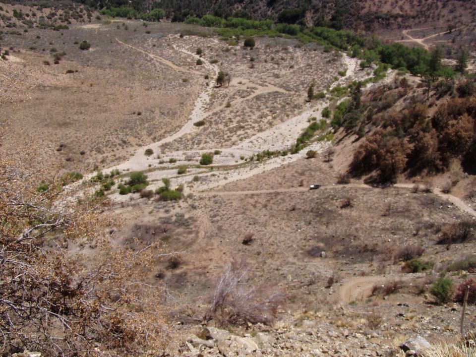 white vehicle drives on a dirt road through a dry, hilly landscape with sparse vegetation