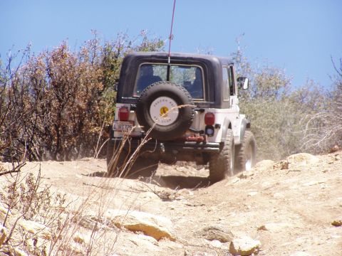 1967 Ford Bronco - A white Jeep Wrangler navigates a dusty, off-road trail under a clear blue sky.