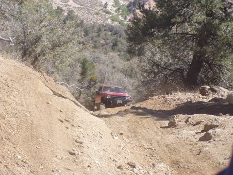 1967 Ford Bronco - A red off-road vehicle navigates a steep, dusty trail in a , natural landscape.