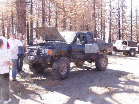 1967 Ford Bronco - A modified black Toyota pickup truck is parked with its hood open, while a white Jeep is visible in the background.