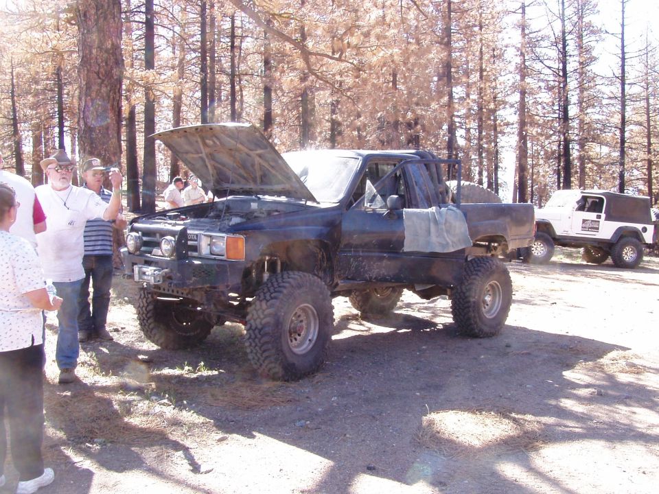 Black Toyota pickup with hood up, big tires, and a white Jeep behind it