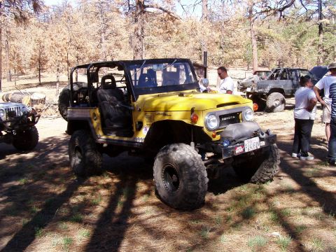 1967 Ford Bronco - A yellow Toyota Land Cruiser FJ40 is parked outdoors with other vehicles and people nearby.