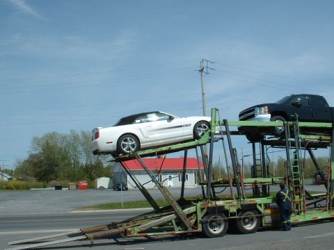 2007 Ford Mustang - A white convertible Mustang and a black pickup truck are being transported on a car carrier.