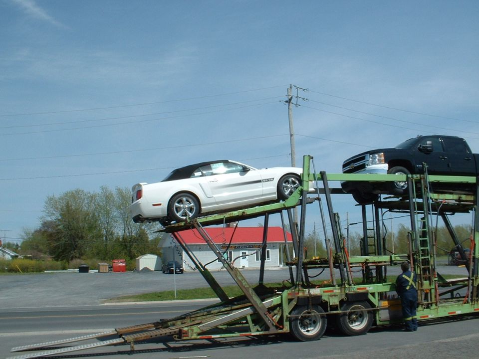 White convertible Mustang and black pickup truck on a car carrier