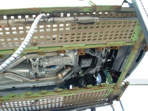 2007 Ford Mustang - The underside of a vehicle is visible, secured to a transport trailer with chains and straps.