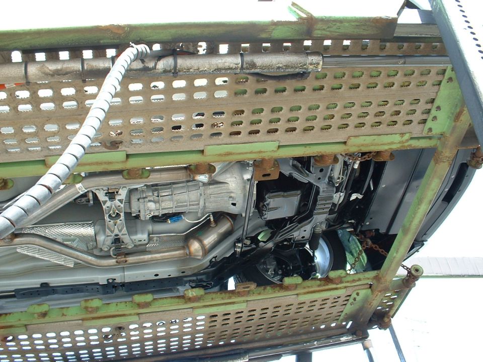 Undercarriage of a car on a green metal trailer, showing transmission, exhaust, and suspension components