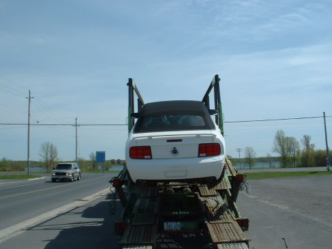 2007 Ford Mustang - A white convertible is being transported on a car hauler, with another vehicle visible on the road.