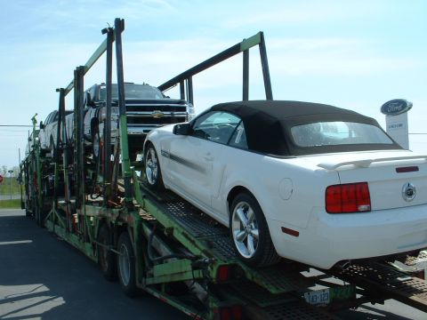 2007 Ford Mustang - Multiple vehicles are transported on a car carrier, including a white convertible Ford Mustang.