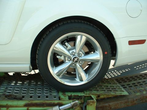2007 Ford Mustang - A close-up view of a chrome wheel and fender of a white vehicle, possibly a Ford Mustang, on a trailer.