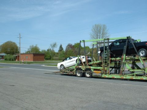 2007 Ford Mustang - A car carrier transports a white 2007 Ford Mustang and a black pickup truck.