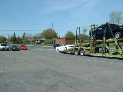2007 Ford Mustang - A car carrier is being loaded with vehicles on a sunny day.