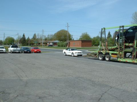 2007 Ford Mustang - A white convertible is being towed by a car carrier, with other vehicles parked nearby.