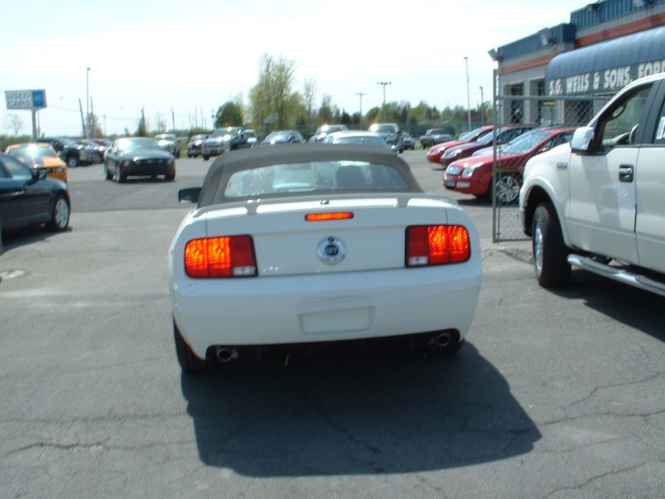 White convertible Mustang from rear, black top, dual exhaust, parked at dealership