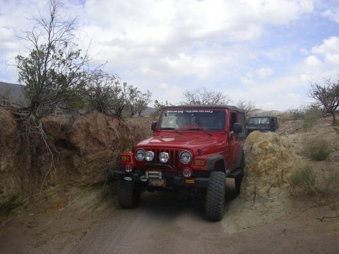 2004 Jeep TJ - Two Jeeps navigate a narrow dirt path with rocky embankments under a cloudy sky.