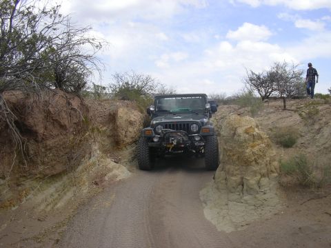 2004 Jeep TJ - A Jeep TJ navigates a narrow dirt path in a desert landscape with a second Jeep following behind.