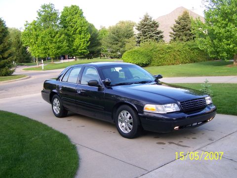 2003 Ford Crown Victoria - A dark-colored sedan is parked on a concrete driveway in a suburban setting. The photo has a timestamp and a website watermark.
