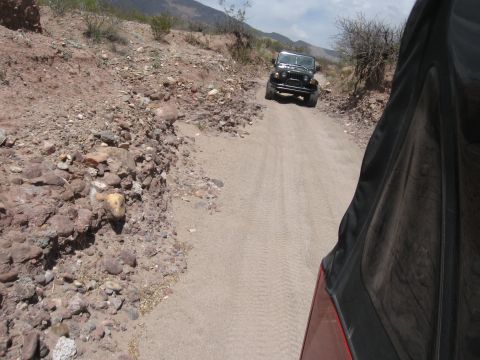 2004 Jeep TJ - A black Jeep TJ navigates a dusty, rocky trail in a desert landscape.