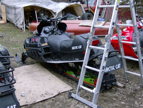 1982 Chevrolet C/K Pickup - An Arctic Cat snowmobile is parked next to a tent, with ladders and another snowmobile in the background.