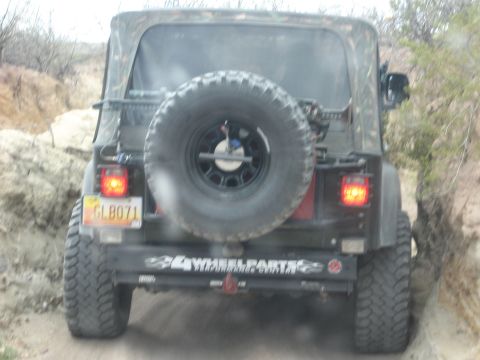 2004 Jeep TJ - Rear view of a black Jeep TJ driving on a dirt trail with rocky terrain.