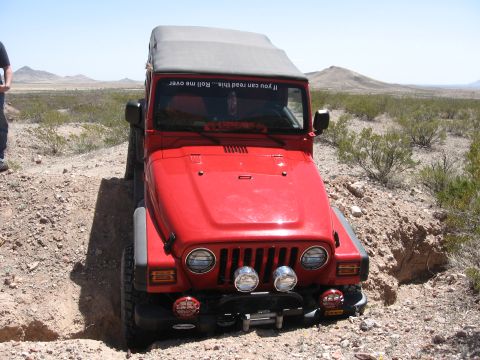 2004 Jeep TJ - This red Jeep Wrangler is navigating a rough off-road trail in a desert landscape.