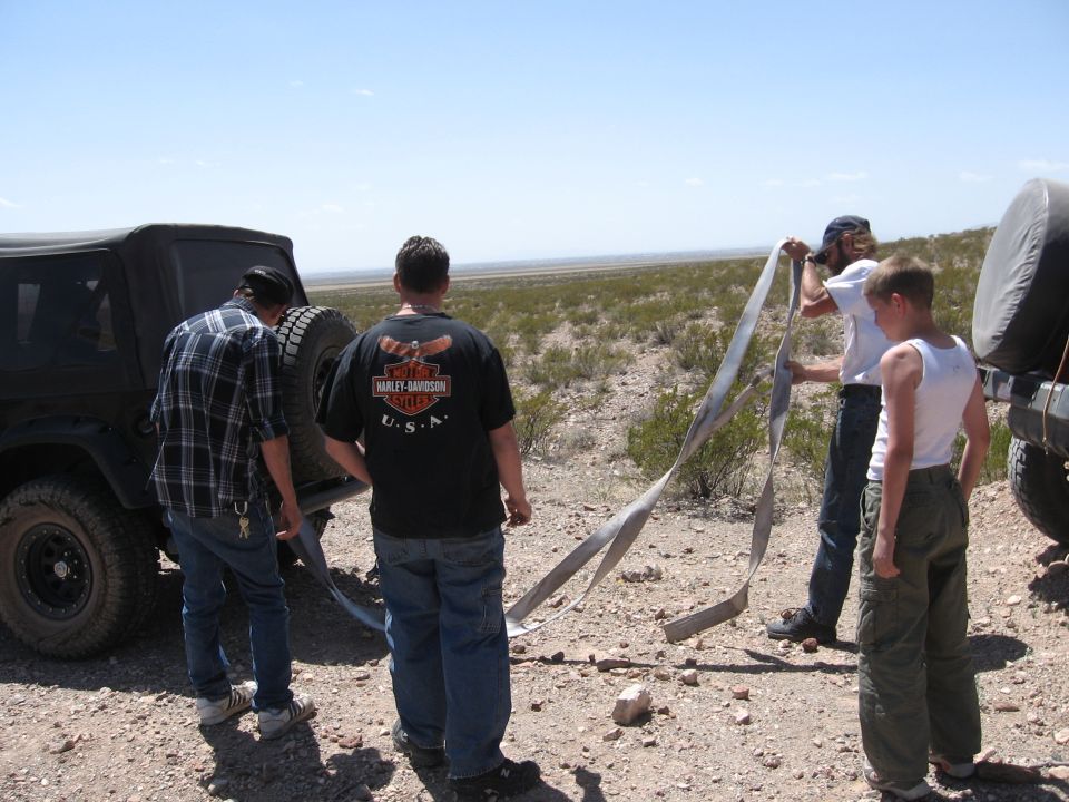 Black Jeep TJ with spare tire on rear, seen from behind with people handling tow straps