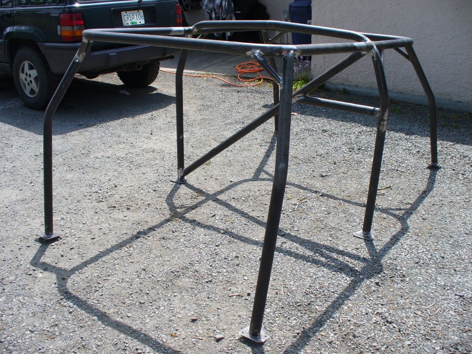 Custom roll cage frame on gravel, with a dark SUV in the background