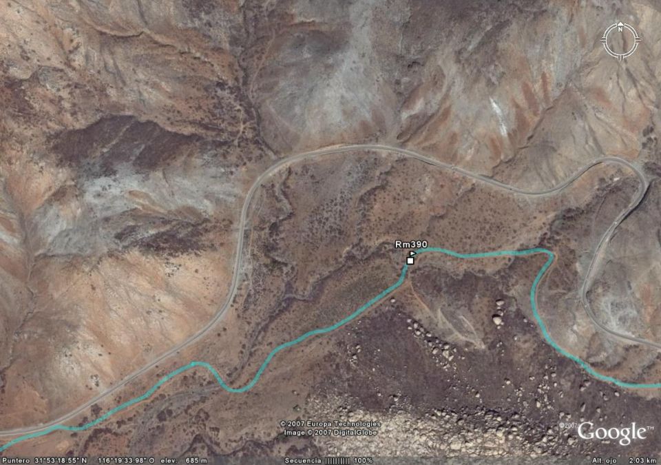 aerial view of a desert landscape with a winding road and a turquoise river, marked with 'Rm 390'