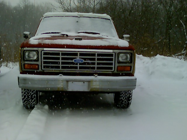 Snow-covered red and white Ford pickup facing camera on snowy road