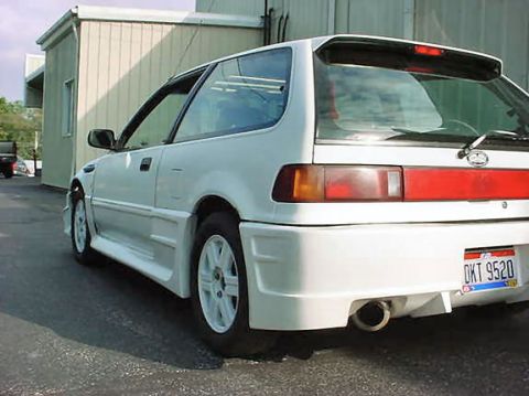 1901 Honda Odyssey - A white hatchback with a sporty body kit is parked outside a building.