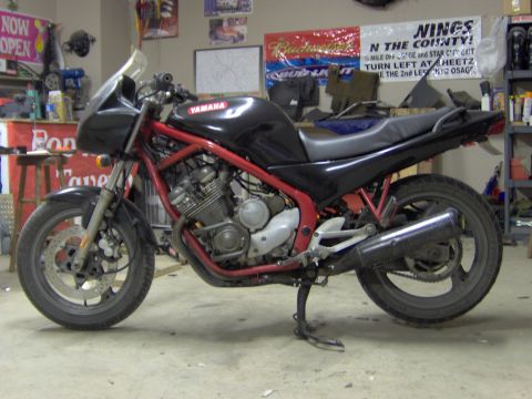 1993 Yamaha Seca II - A Yamaha motorcycle with a black fuel tank and red frame is parked indoors, with various signs and items on the wall behind it.