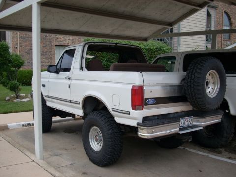 1992 Ford Bronco - A white 1992 Ford Bronco is parked under a carport, showing its rear and side profile with a spare tire on the back.