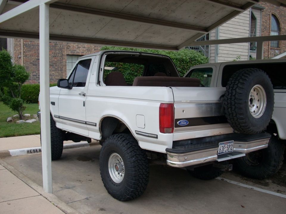 White 1992 Ford Bronco with a spare tire mounted on the rear, parked under a carport