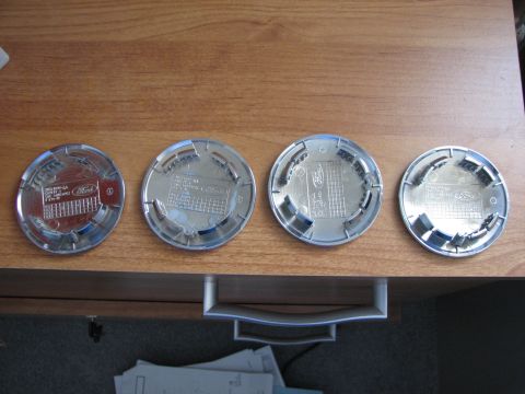 2003 Ford Crown Victoria - Four Ford wheel center caps are displayed on a wooden surface, revealing their part numbers and the Ford branding.