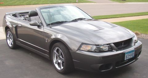 1993 Ford Bronco - A gray Ford Mustang convertible is parked on a driveway, showing its front three-quarter view.