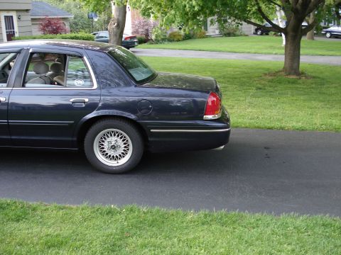 2000 Ford Crown Victoria - Rear three-quarter side view of a dark blue full-size Ford sedan parked on a residential asphalt driveway, showing the rear door, fuel fill…