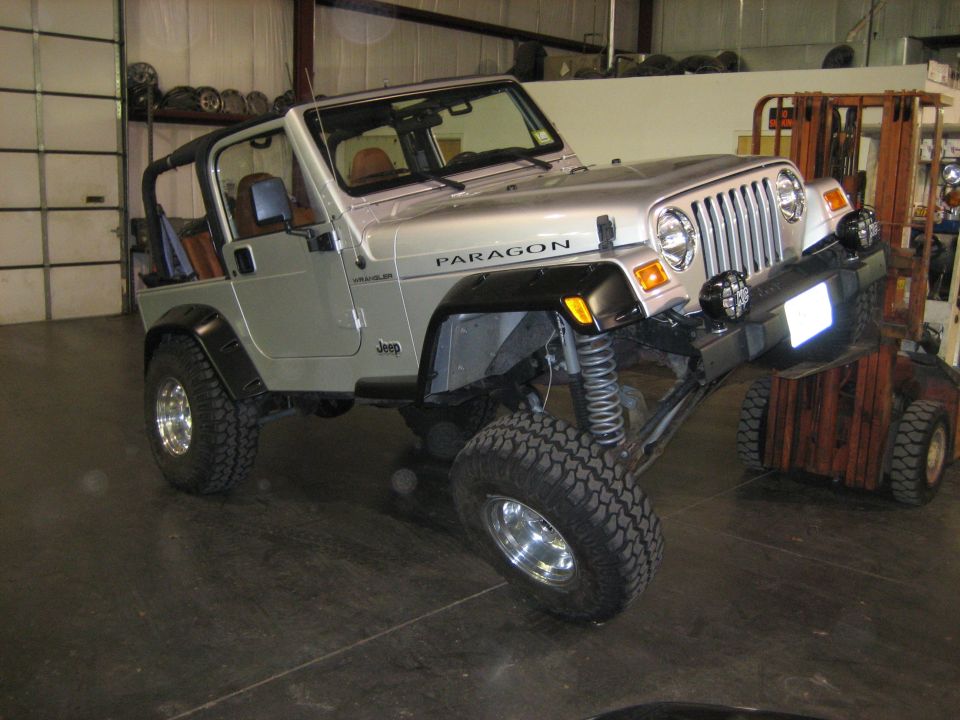 Silver Jeep Wrangler with a lift kit, front end raised by a forklift
