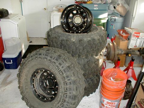1996 Ford Bronco - Off-road tires and wheels are stacked in a garage, with a rear axle assembly visible.