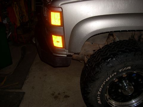 2000 Chevrolet Tahoe - Close-up of a silver truck's front corner, showing the turn signal lights and a large tire. The vehicle's body style suggests a 1990s model.