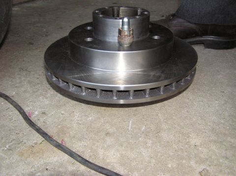 2000 Chevrolet Tahoe - A new brake rotor is shown on a concrete surface, with a lug nut secured to its center.