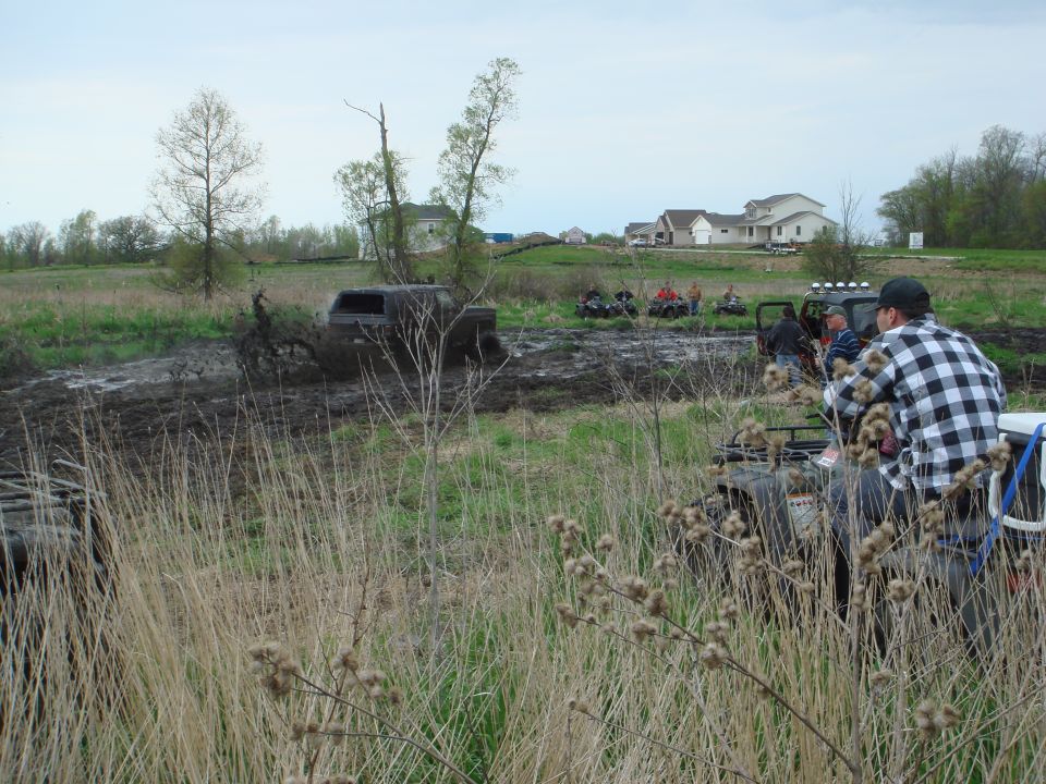 Spectators on ATVs watch a truck mudding in a field