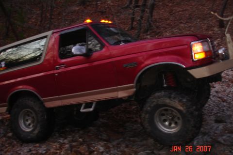 1995 Ford Bronco - This red 1995 Ford Bronco is shown on a trail with lifted suspension and off-road tires.