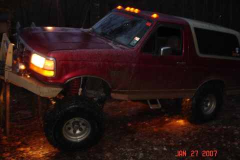 1995 Ford Bronco - This lifted 1995 Ford Bronco is shown with its lights on, parked on a wet surface at night.